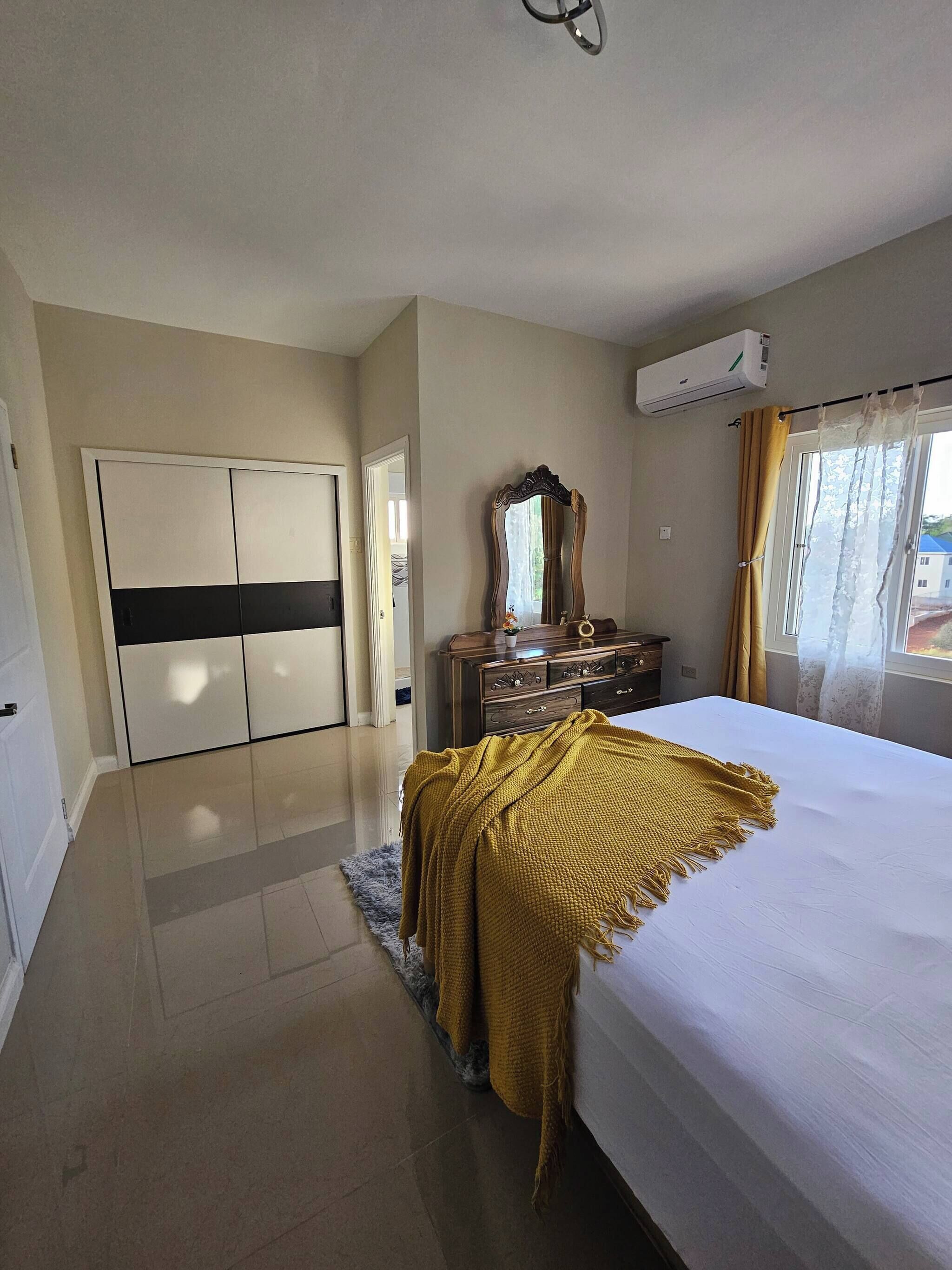 Un dormitorio con cama, armario, cómoda, espejo y aire acondicionado.