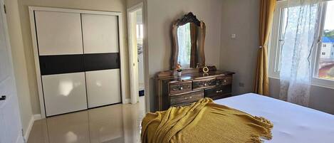 Un dormitorio con cama, armario, cómoda, espejo y aire acondicionado.