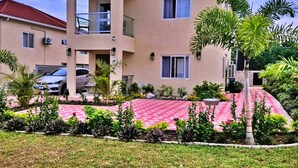A two-story building with a balcony, a carport, and a landscaped garden with palm trees. - Tranquility Loft, Ocho Rios, Solar Powered (Ocho Rios)