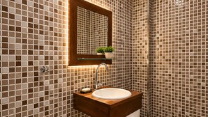 A bathroom with a tiled wall, a sink, a mirror, a toilet, and a showerhead. - Studio apartment in the city center with Wi-Fi. (Manaus)