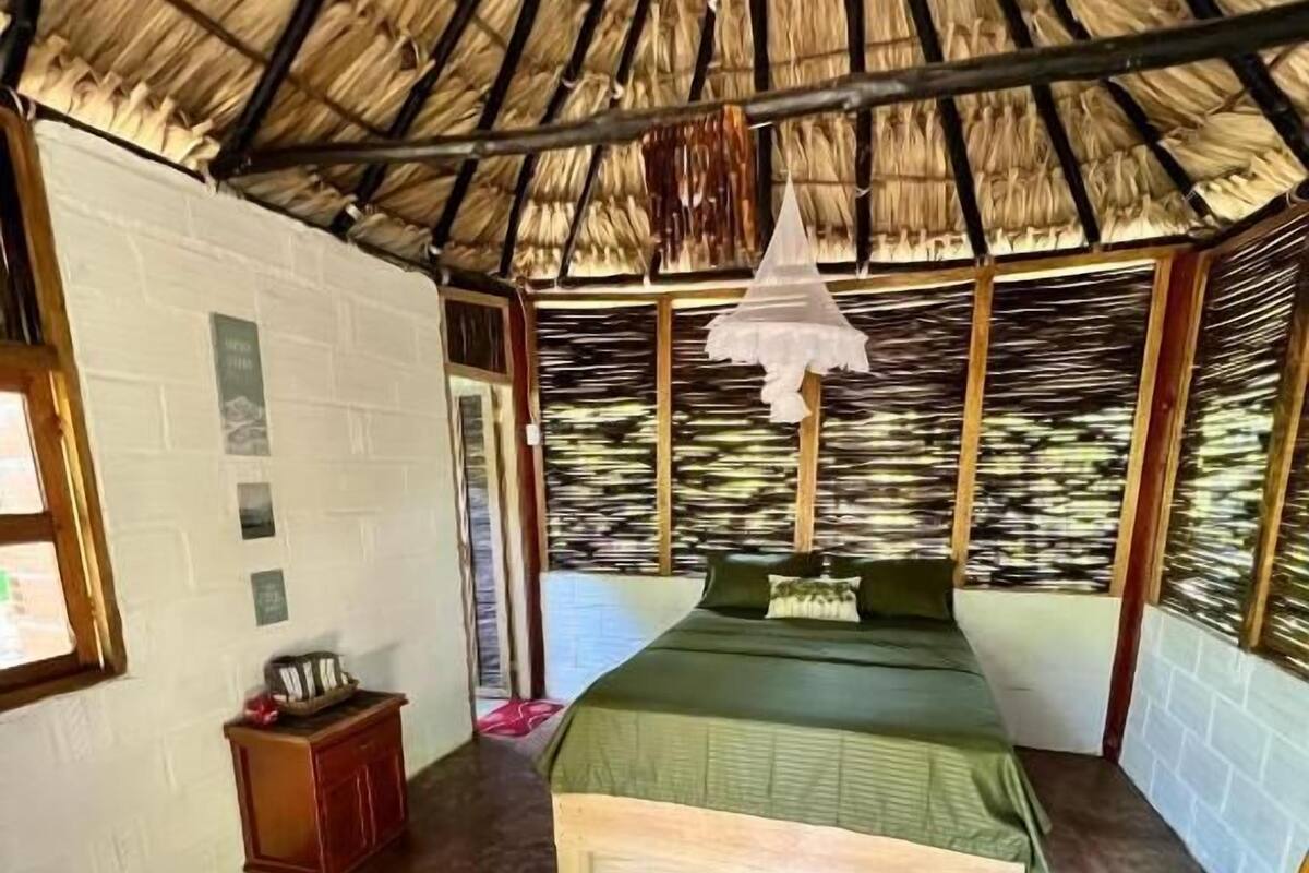 Ein Zimmer mit einem Bett, einem kleinen Holzschrank und einem Strohdach.