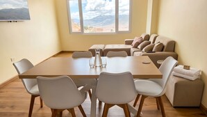 Un soggiorno moderno con un tavolo da pranzo, sedie bianche, un divano e vista sulle montagne dalla finestra.