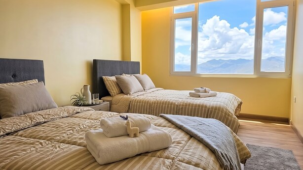 Ein Hotelzimmer mit zwei Betten, einem großen Fenster mit Blick auf die Berge und einem Nachttisch mit einer Karaffe und einem Glas.