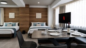 A hotel room with two beds, a dining table set for four, a flat-screen TV, and a bottle of wine. - Ebisu City Stay (Tokyo)