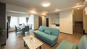 A modern living room with a sofa, dining area, kitchen, and staircase. - Ebisu City Stay (Tokyo)