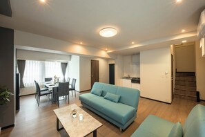A modern living room with a sofa, dining area, kitchen, and staircase.