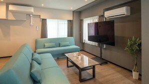 A modern living room with a sofa, a coffee table, a flat-screen TV, and an air conditioning unit. - Ebisu City Stay (Tokyo)