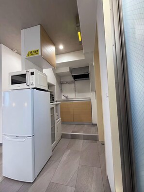 A compact kitchen with a refrigerator, microwave, and wooden cabinets.