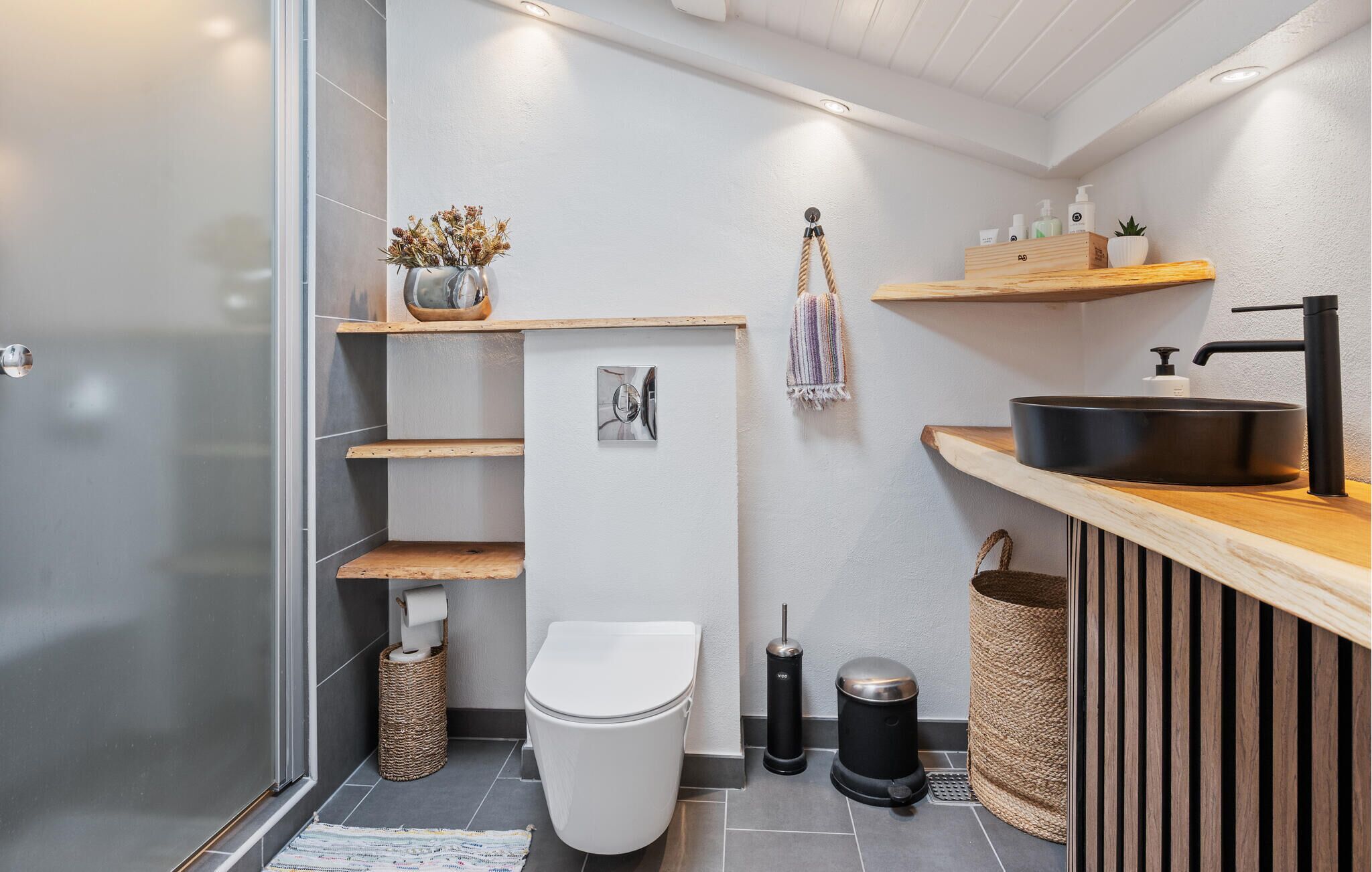 A modern bathroom with a toilet, sink, and shelves.