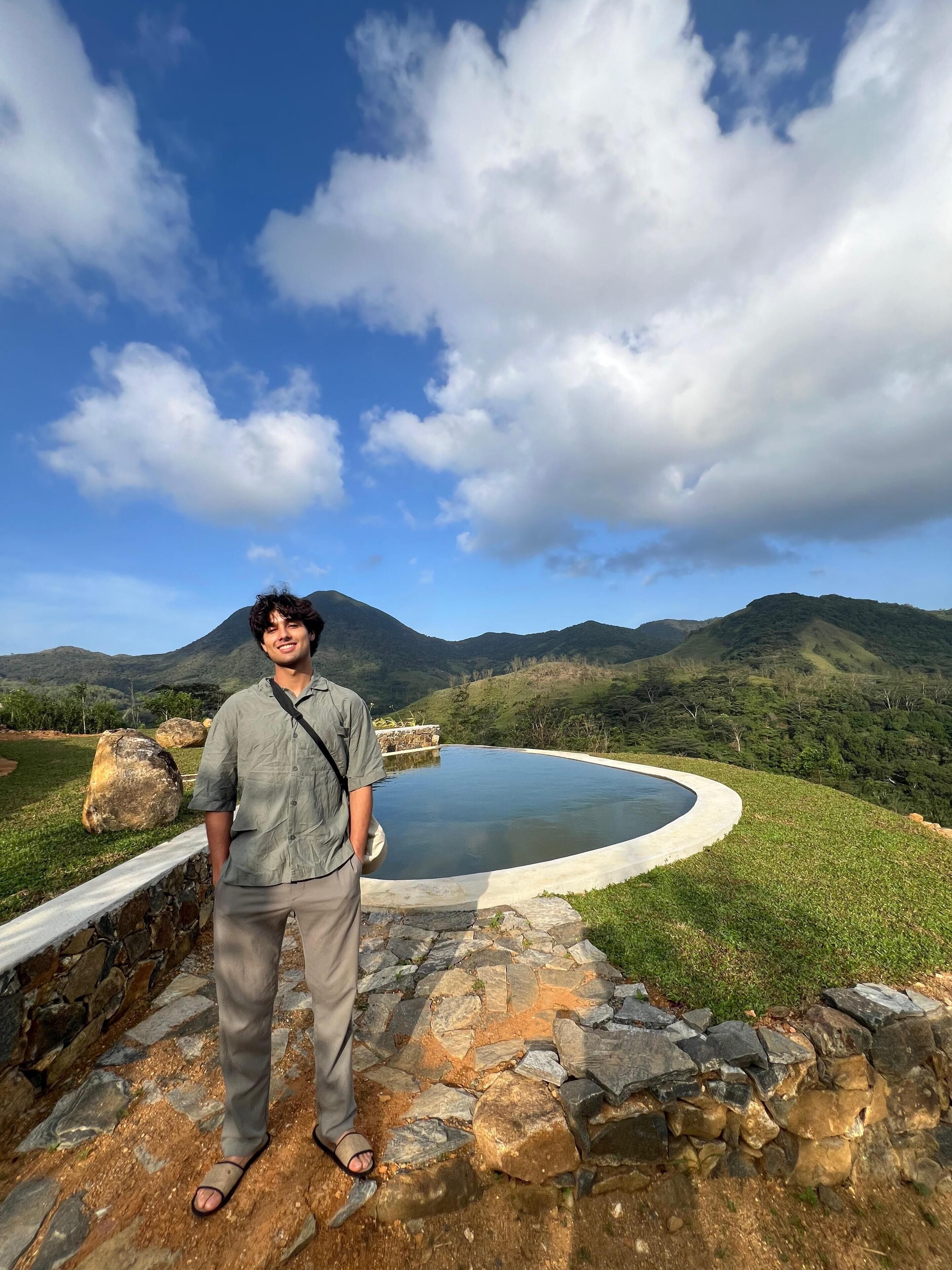 A person standing by a stone pool with a mountainous landscape in the background.