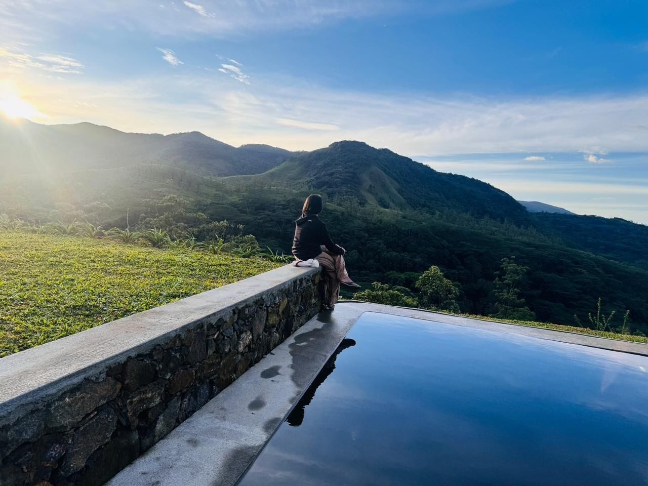 Una persona sentada en un borde de piedra con vistas a un paisaje montañoso.