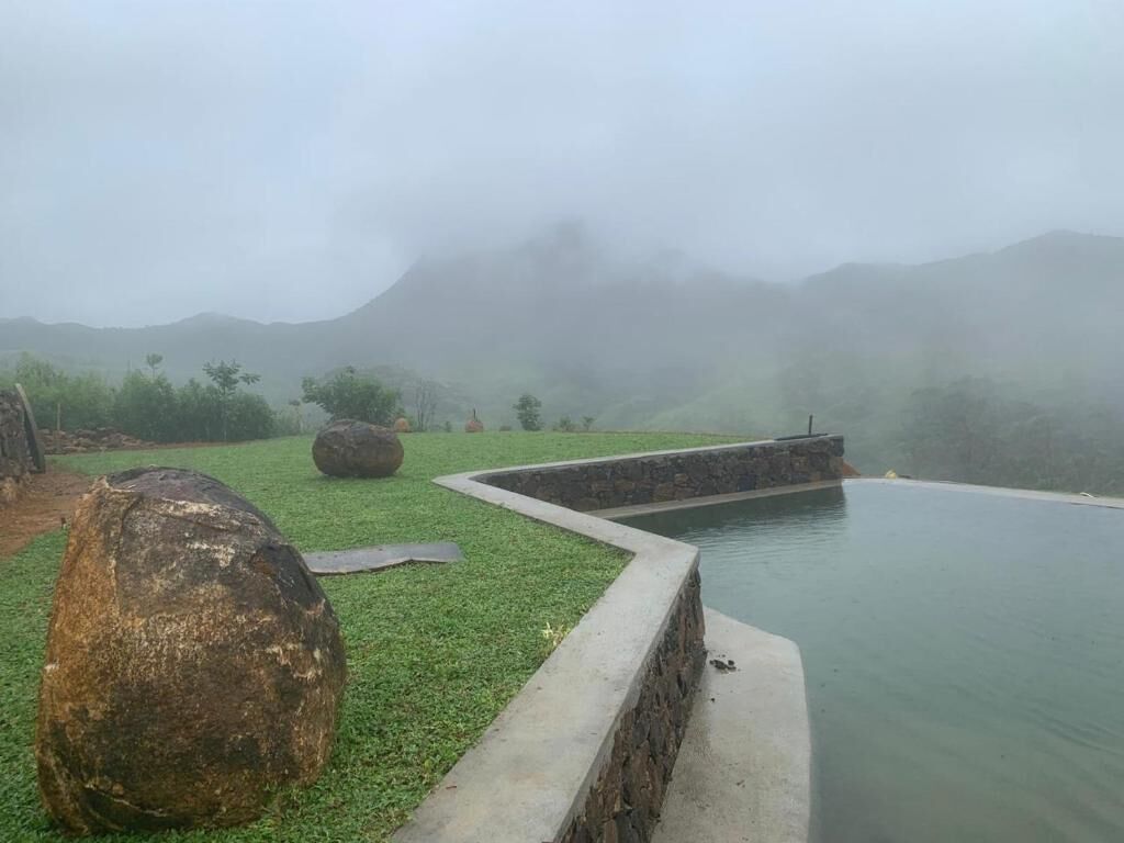 A tranquil pool area with a stone border, a large rock, and a grassy foreground.