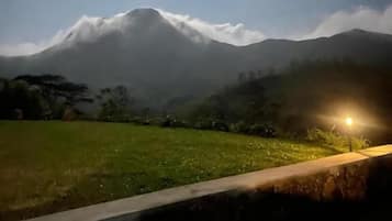 A mountain landscape with a grassy field and a stone wall in the foreground.