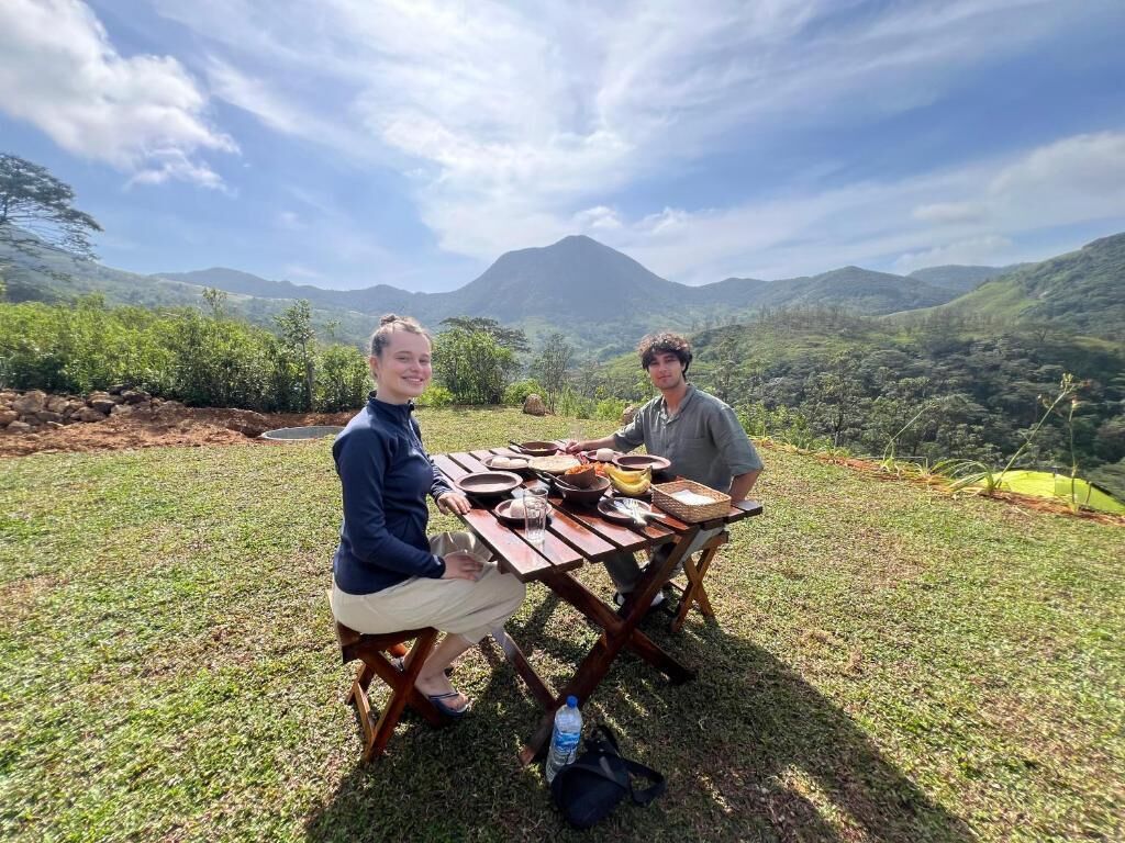 Twee personen zitten aan een buitentafel met een berg in de verte.
