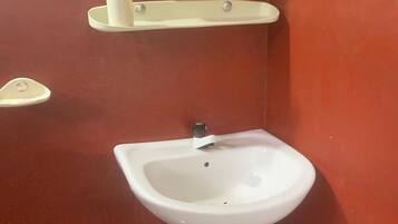 A white pedestal sink with a mirror above it, a soap dispenser, and a towel holder on a red wall.