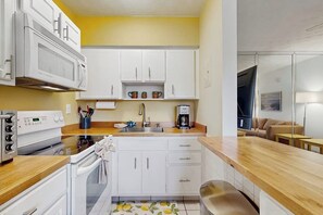 A compact kitchen with white cabinets, a microwave, a stove, and a coffee maker.