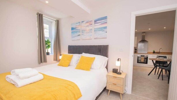 A bedroom with a bed, bedside tables, a nightstand, a window with curtains, a view of the kitchen, and a dining area. - Cosy Chic 1BR Haven in Hull Centre Near Marina (Hull)