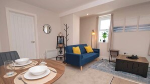 A living room with a dining table set, a blue sofa, a small side table, and a radiator. - Cosy Chic 1BR Haven in Hull Centre Near Marina (Hull)