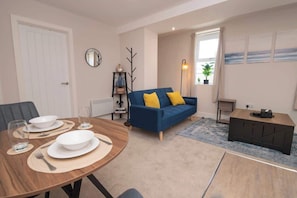 Ein Wohnzimmer mit Essplatz, einem blauen Sofa, einem kleinen Beistelltisch und einer Heizung.