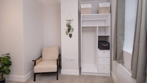 A room with a chair, a white closet with shelves, a hanging plant, and a window with curtains. - Cosy Chic 1BR Haven in Hull Centre Near Marina (Hull)