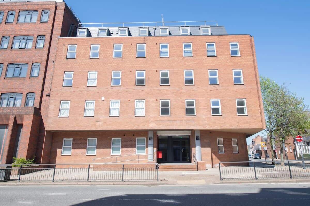 A multi-story brick building with a flat roof, large windows, and a gated entrance.