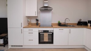 A modern kitchen with white cabinets, a stainless steel range hood, a built-in oven, and a wooden countertop. - Cosy Chic 1BR Haven in Hull Centre Near Marina (Hull)