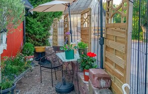 Un jardín con mesa y sillas, plantas en macetas, cerca de madera y pared roja.
