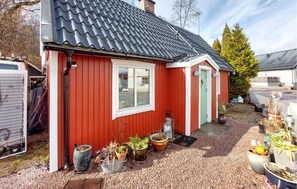 A red building with a black roof, a window, and a door. There are potted plants outside.
