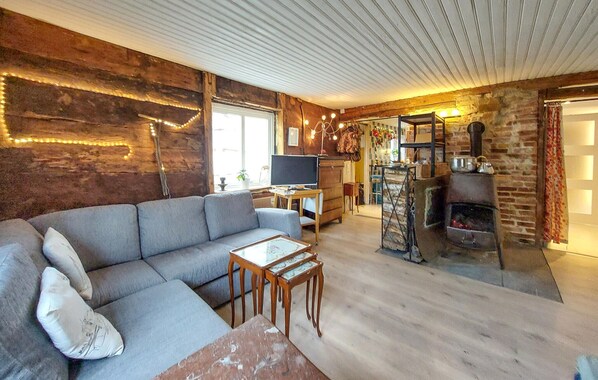 A cozy living room with a sofa, a television, a fireplace, and a rustic wooden wall.