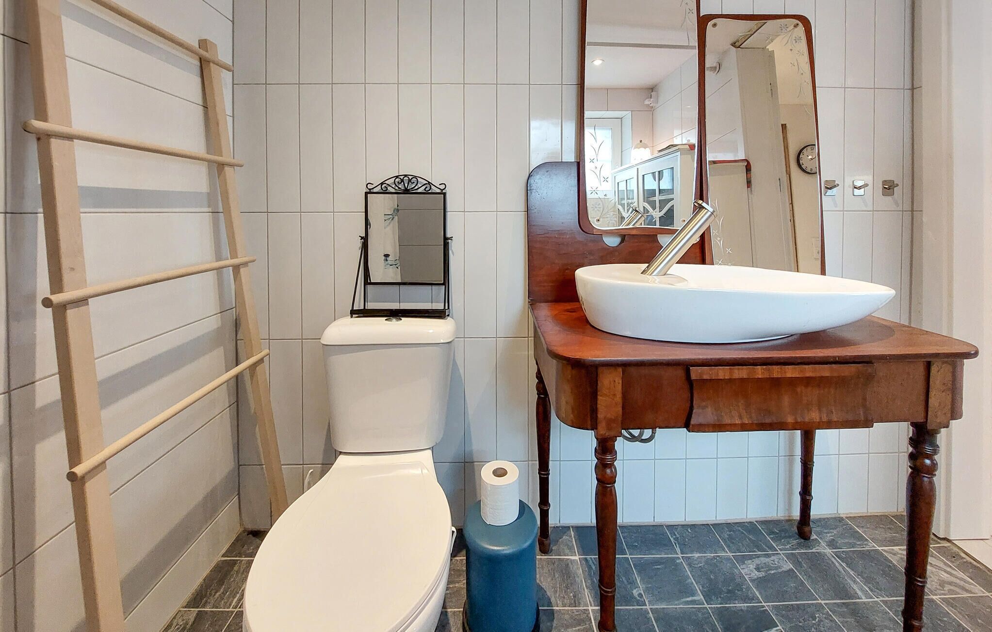 A bathroom with a toilet, a sink on a wooden vanity, a mirror, and a towel rack.