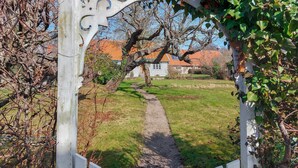 Un sendero en un jardín que lleva a una casa con cerca blanca y un arco decorativo.