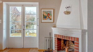 Una habitación con una chimenea blanca, una puerta con paneles de vidrio y un cuadro en la pared.