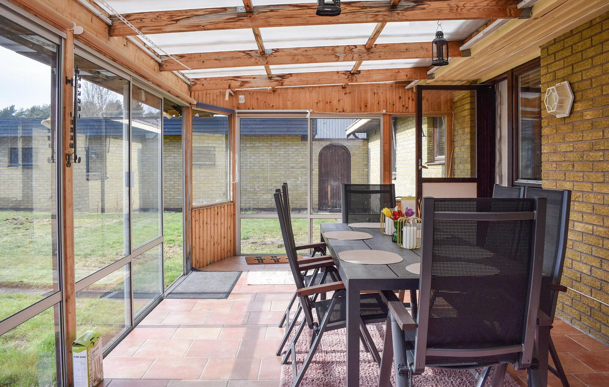 Une terrasse couverte avec une table et des chaises, de grandes fenêtres et un mur en briques.
