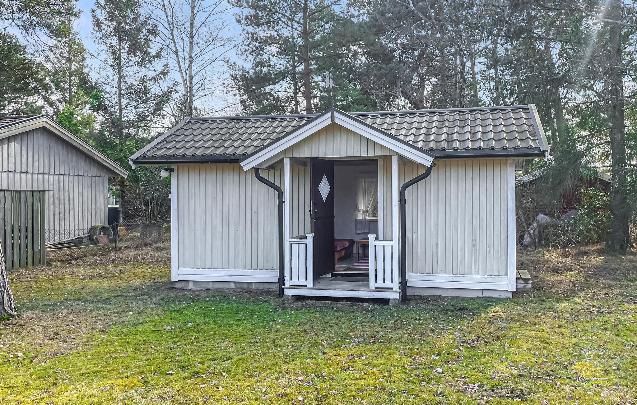 Eine kleine, eingeschossige Holzhütte mit Veranda, umgeben von Bäumen.