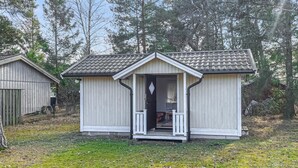 A small, single-story wooden cabin with a porch, surrounded by trees.
