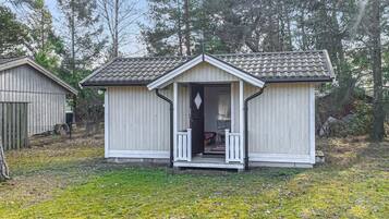 Eine kleine, eingeschossige Holzhütte mit Veranda, umgeben von Bäumen.