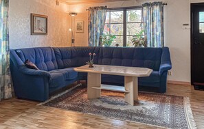 A room with a blue sofa, a small table, a patterned rug, and a window with curtains.