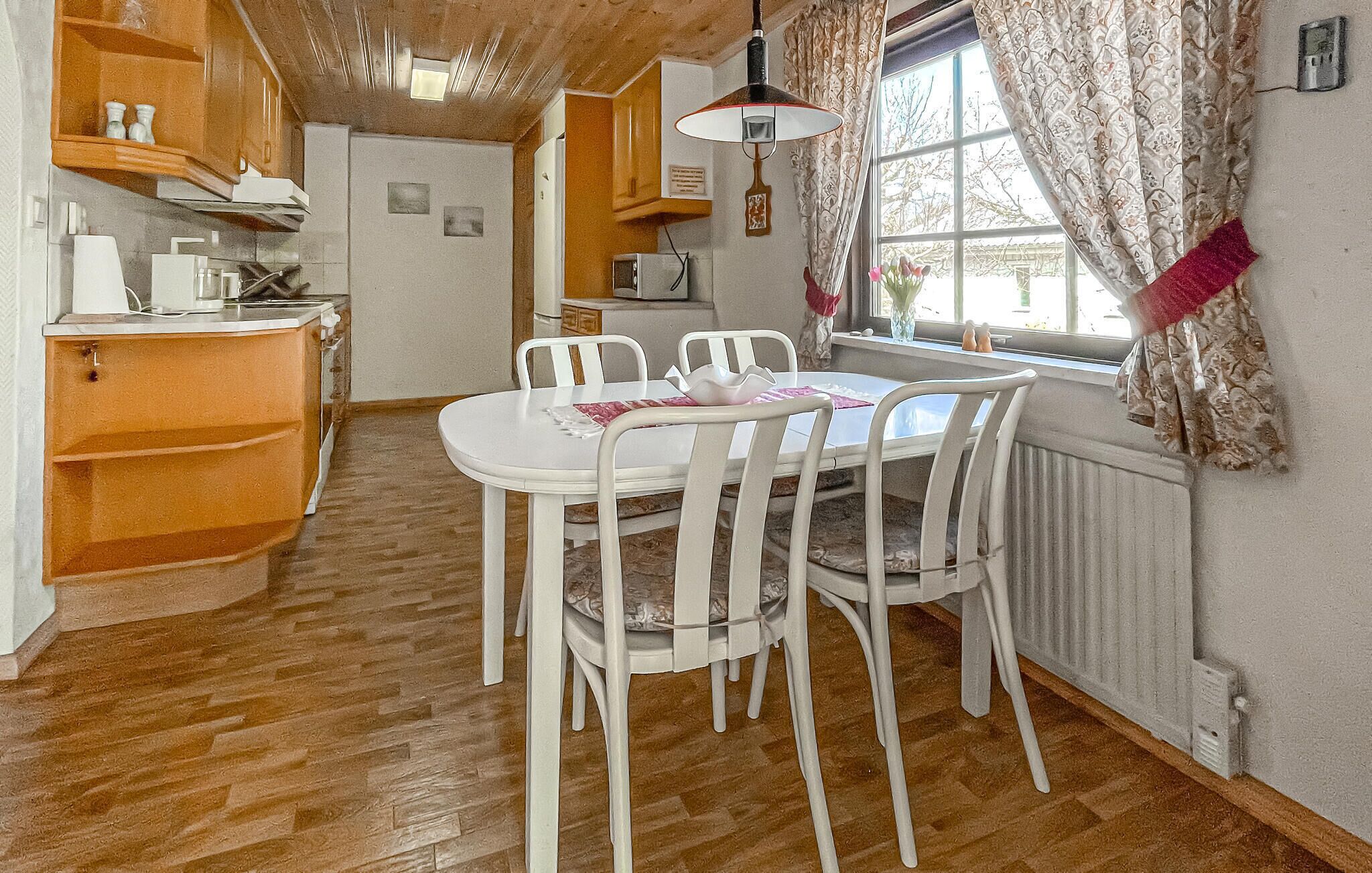 A compact kitchen with a dining table, chairs, and a window with curtains.