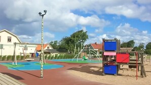 A playground with a climbing structure, a swing set, and a basketball court.