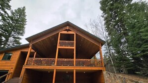 Een houten chalet met twee verdiepingen, een balkon op de bovenverdieping, een stenen keerwand en een oprit naar de ingang.