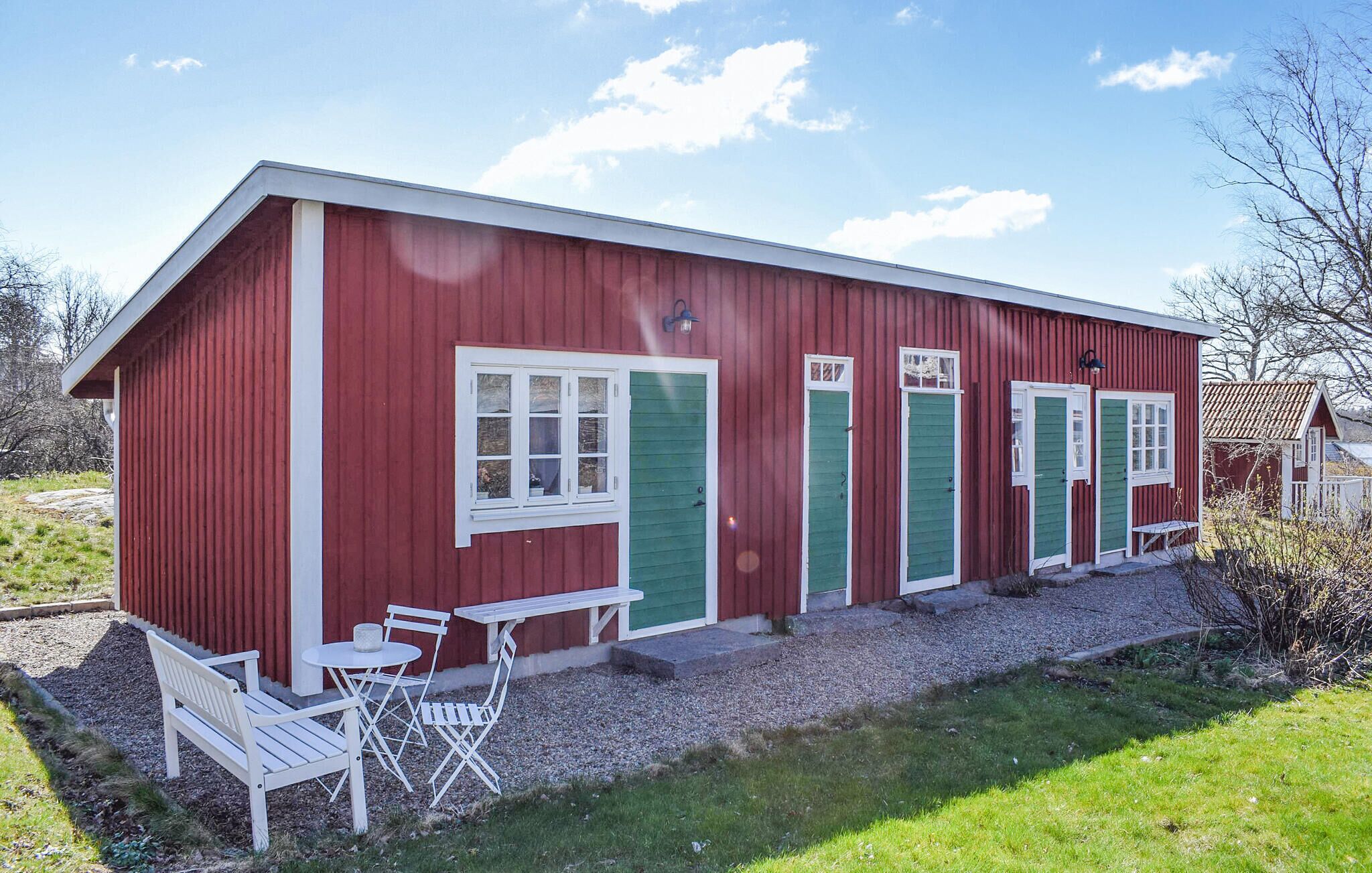 A red building with green doors and windows, a bench, and a table outside.