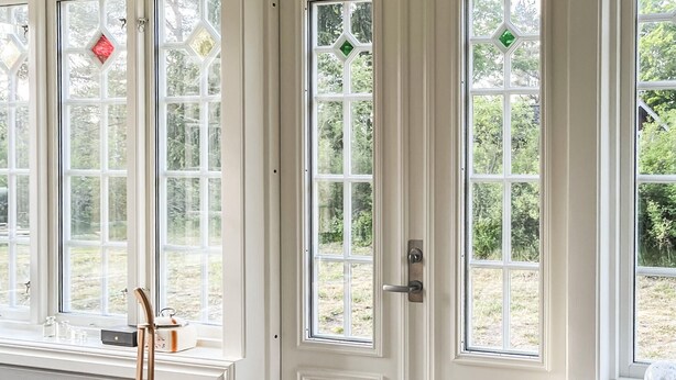 Une paire de portes doubles blanches, dotées de panneaux de verre, chacune ornée d’un vitrail en forme de losange.