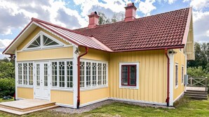 Une maison jaune avec un toit recouvert de tuiles rouges, une grande baie vitrée et un petit porche à l’avant.