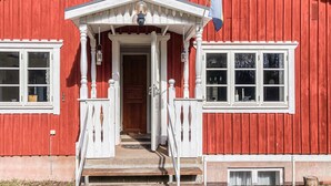 Un edificio de madera roja con un porche blanco, una bandera y una puerta.