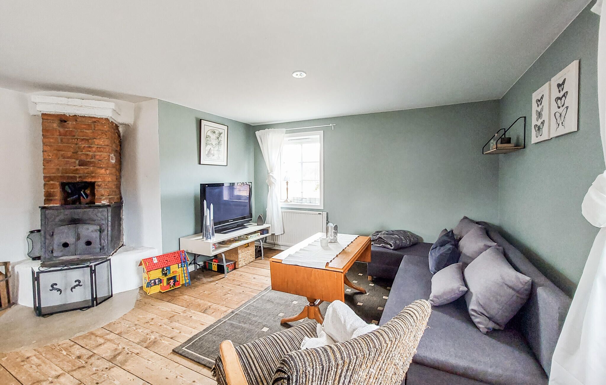 Ein Wohnzimmer mit Fernseher, Kamin, Sofa und einem fensterbehangenen Fenster.