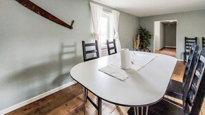 Een eethoek met een ronde tafel, stoelen, een hangende zaag en een raam met gordijnen.