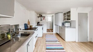 Een smalle keuken met witte kastjes, een roestvrijstalen spoelbak, een magnetron en een houten vloer.