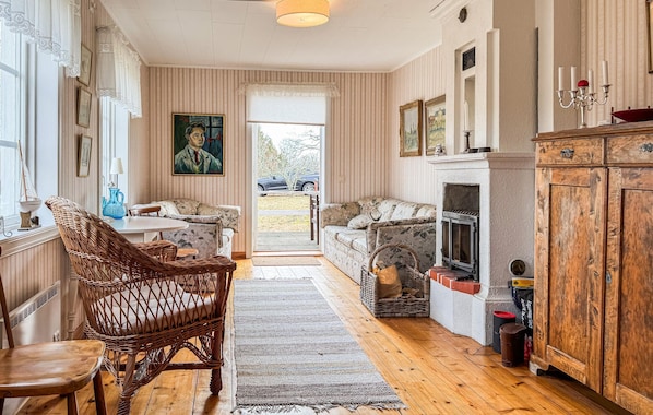 Ein gemütliches Wohnzimmer mit Kamin, Korbmöbeln und Blick durch eine Tür.