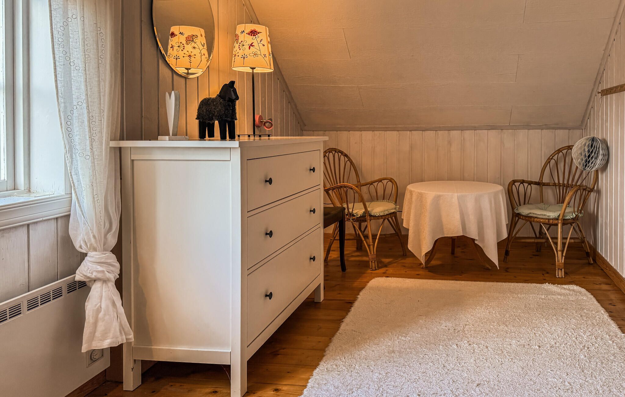 A cozy room with a white dresser, two chairs, a round table, and a white rug.
