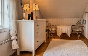 Ein gemütliches Zimmer mit einer weißen Kommode, zwei Stühlen, einem runden Tisch und einem weißen Teppich.